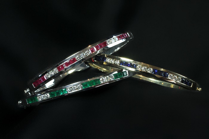 Three bangle bracelets set with square cut rubies, sapphires and emeralds alongside round cut diamonds